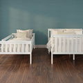 Two white twin beds with neutral bedding and striped throw pillows against a teal accent wall on dark hardwood flooring