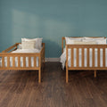 Two wooden twin beds with white bedding and beige striped pillows against a teal textured wall on dark hardwood flooring