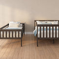 Dark wood twin beds with blue-and-white floral pillows and light blue bedding in a neutral kids' bedroom with hardwood floors and beige walls