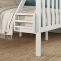 White wooden loft bed ladder and slatted guardrail beside beige linen bedding with fringed throw on a textured woven jute rug