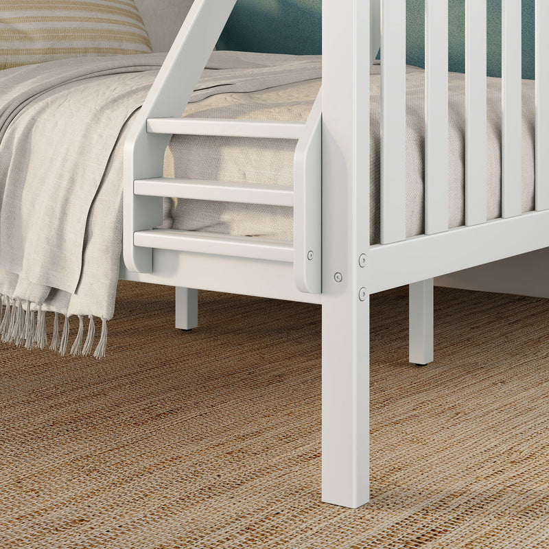 White wooden loft bed ladder and slatted guardrail beside beige linen bedding with fringed throw on a textured woven jute rug