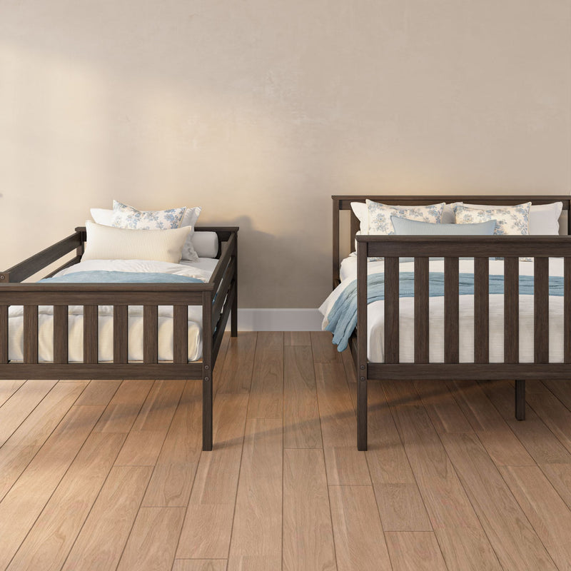 Two dark wooden twin beds with light blue bedding and floral pillows against a neutral beige wall in a minimalist bedroom with hardwood floors.