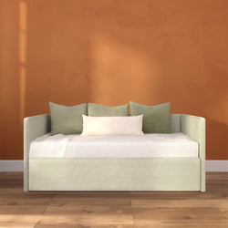 Modern neutral daybed sofa with sage-green cushions and white throw pillow against a terracotta accent wall on hardwood floor