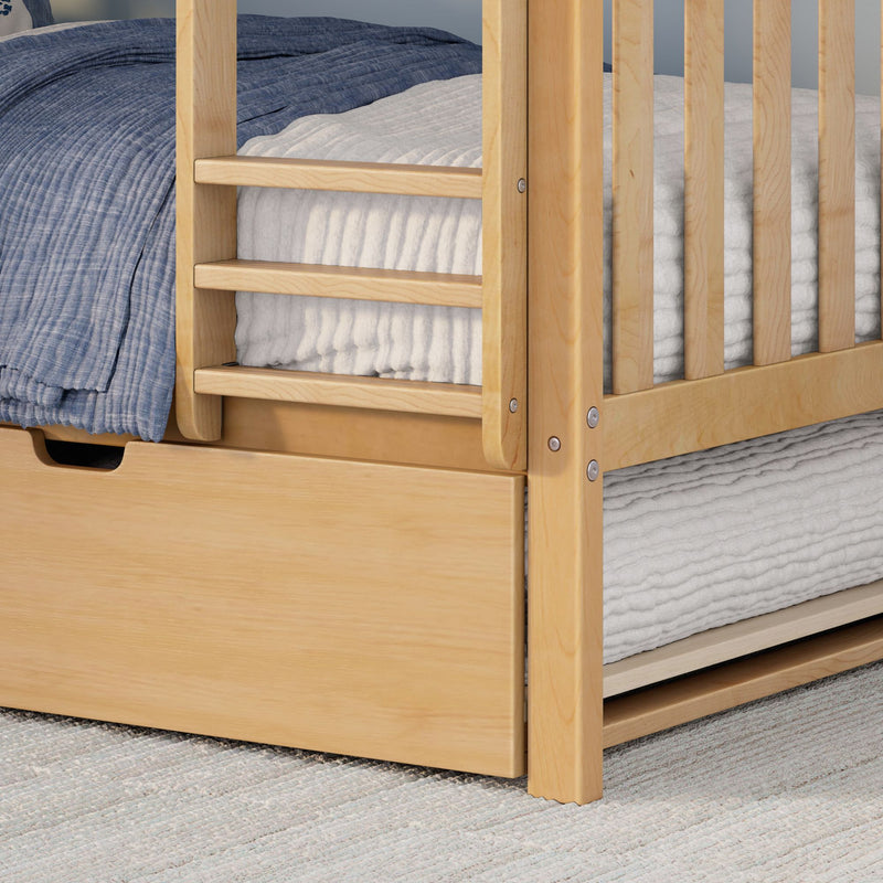 Close-up of light wood bunk bed frame and guardrail with blue quilt, white textured bedding and under-bed trundle drawer.