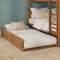 Wooden twin bunk bed with pull-out trundle, neutral linen bedding and striped pillows against a teal textured wall with a woven jute rug