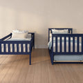 Two navy blue twin beds with white and blue floral pillows in a minimalist kids' bedroom with light beige wall and hardwood floor.