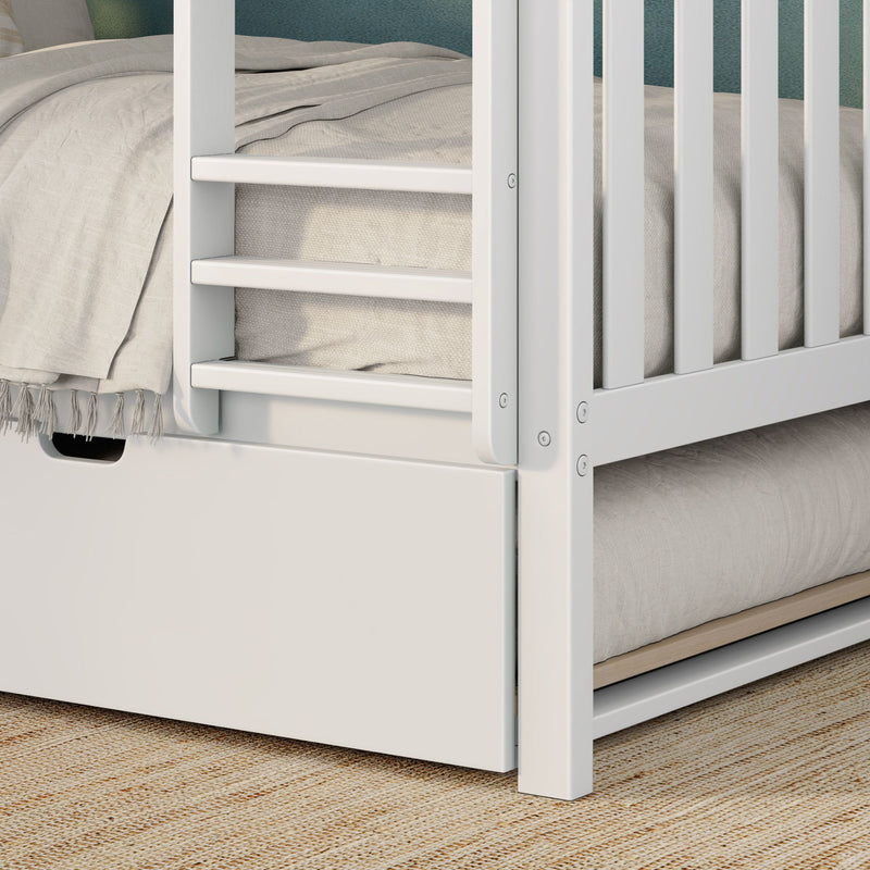 Close-up of modern white wooden bunk bed ladder and safety guardrail with light gray bedding, tassel throw, storage drawer cutout and woven jute rug