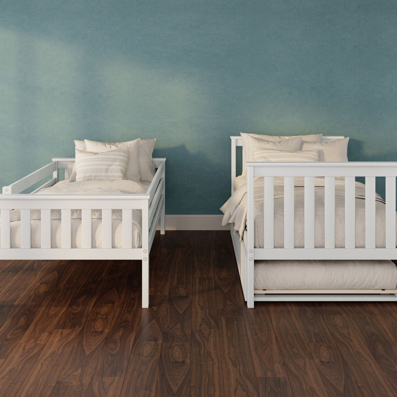 Two white wooden twin beds with beige bedding and striped pillows against a textured teal accent wall and dark hardwood floor