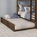 Wooden bunk bed with blue and white bedding and leaf-print accent pillow over pull-out trundle on textured rug