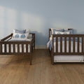 Two wooden twin beds with blue leaf-print pillows and white quilts on a hardwood floor against a light blue bedroom wall