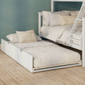 White bunk bed with pull-out trundle, beige linen bedding and striped throw pillows against a teal accent wall on a natural jute rug
