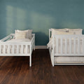 Minimalist children's bedroom with two white wooden twin beds, neutral striped pillows, teal textured accent wall and dark hardwood floor