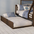 Wooden bunk bed with pull-out trundle, white quilted bedding and blue decorative pillows on a textured beige rug
