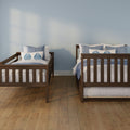 Two wooden twin beds with blue-and-white bedding in a coastal-style bedroom with a light blue wall and hardwood floor