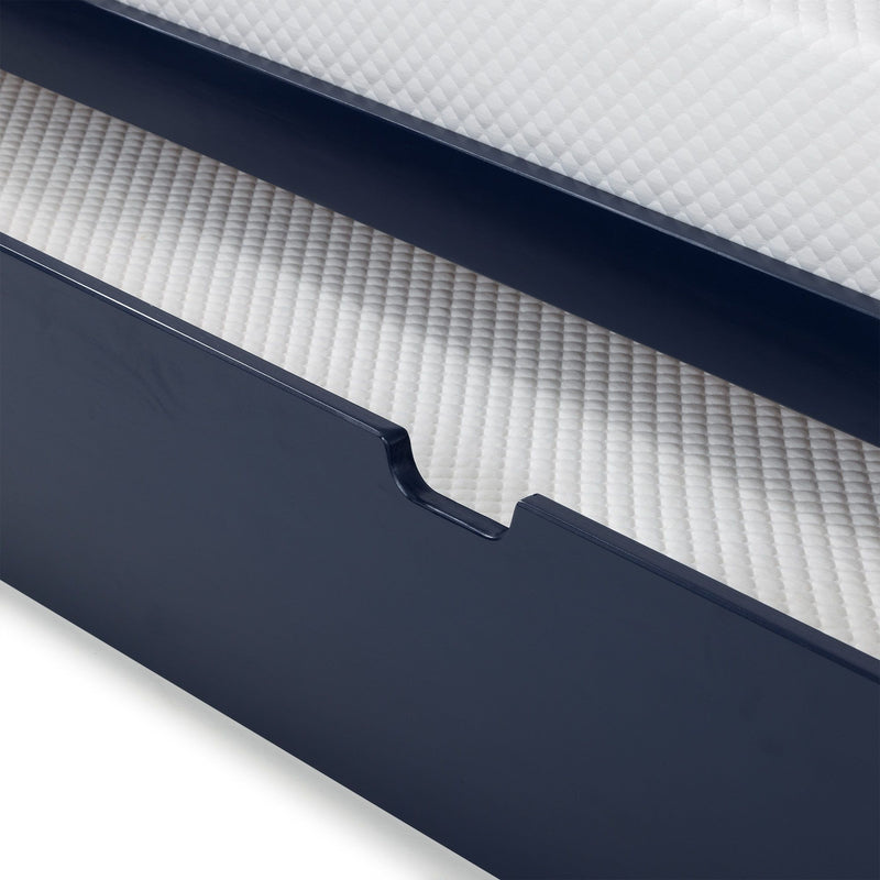 Close-up of navy blue wooden bed frame with scalloped drawer front and white quilted mattress on a textured pad