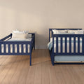 Navy blue twin beds with white and floral pillows in a cozy beige-walled bedroom with light hardwood flooring