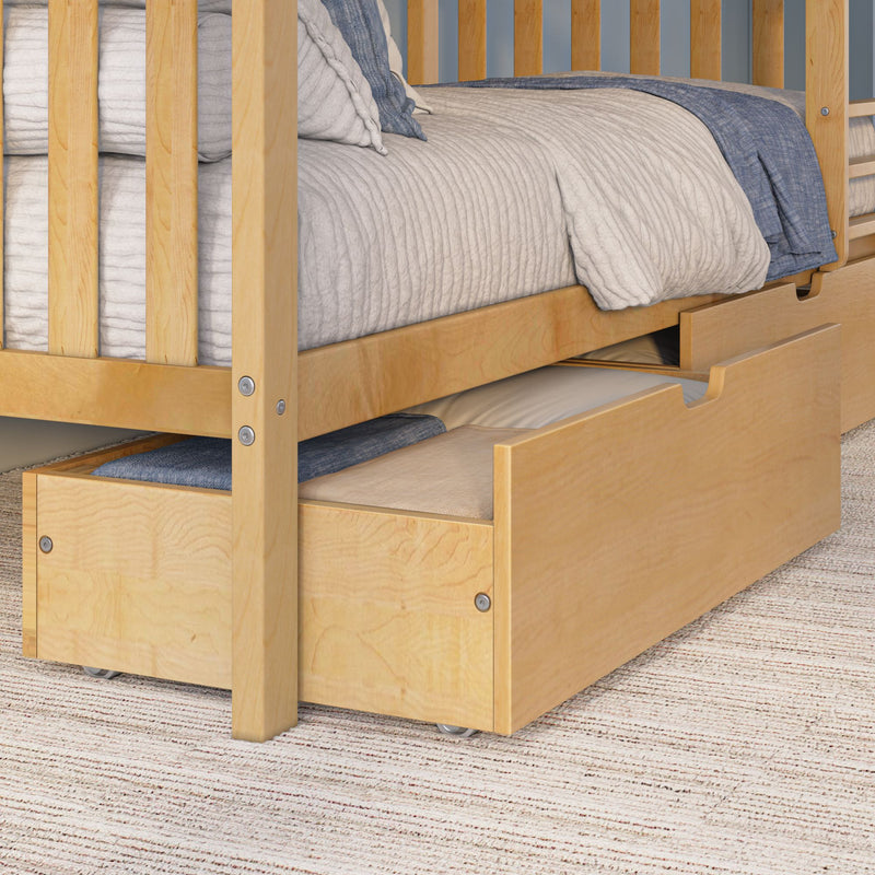 Close-up of wooden bunk bed with pull-out trundle storage drawer, beige quilted bedding and blue throw on maple-finish frame