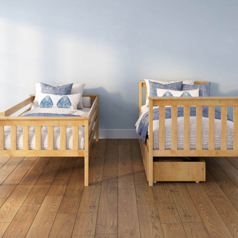 Two wooden twin beds with blue and white bedding and leaf-pattern pillows against a light blue wall on a hardwood floor