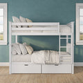 White wooden twin-over-twin bunk bed with storage drawers, neutral linen bedding and plaid accent pillows against a teal textured wall in a bright coastal-style kids' bedroom