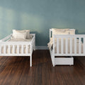 Two white wooden twin beds with beige bedding and striped pillows in a kids' bedroom with teal textured wall and dark hardwood floor