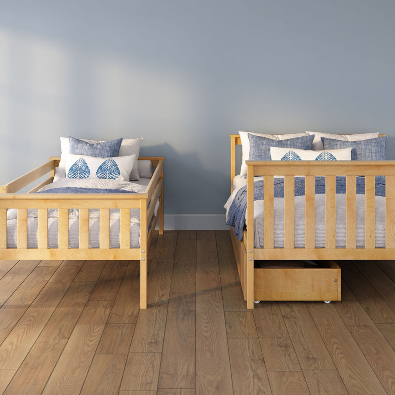 Two wooden twin beds with blue-and-white bedding and leaf-print pillows in a minimalist kids bedroom with hardwood floor and under-bed storage drawer