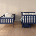 Two navy blue twin beds with floral pillows and light blue bedding in a cozy children's bedroom with beige walls, hardwood floor and under-bed storage drawer