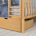 Light maple bunk bed with pull-out storage drawer, slatted safety rails and blue quilted bedding on textured rug
