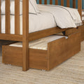 Solid wood bunk bed with pull-out trundle drawer, white bedding and folded blanket, warm wood finish on woven jute rug