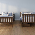 Two dark wood twin beds with blue and white bedding and pillows against a pale blue wall on a hardwood floor, bedroom interior