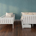 Two white wooden twin beds with neutral bedding against a teal textured wall and dark hardwood flooring in a kids' bedroom.