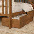 Solid wood twin trundle bunk bed with warm wood finish, beige linen bedding and under‑bed storage drawer on woven rug — space‑saving kids bedroom solution