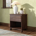 Dark wood nightstand with white ceramic table lamp and two decorative vases on hardwood floor against a green textured wall and wooden window, bedroom decor