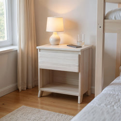 Wooden bedside table with a lamp, smartphone, and glass of water in a cozy bedroom.