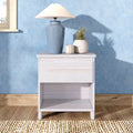 Blue ceramic table lamp on white nightstand with small vases, candle and potted plant against a light-blue textured wall