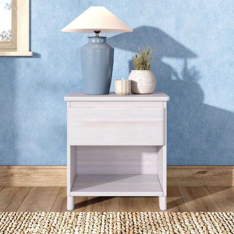 Blue ceramic table lamp on white nightstand with small vases, candle and potted plant against a light-blue textured wall