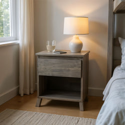 Wooden bedside table with lamp, glass of water, and smartphone in cozy bedroom.