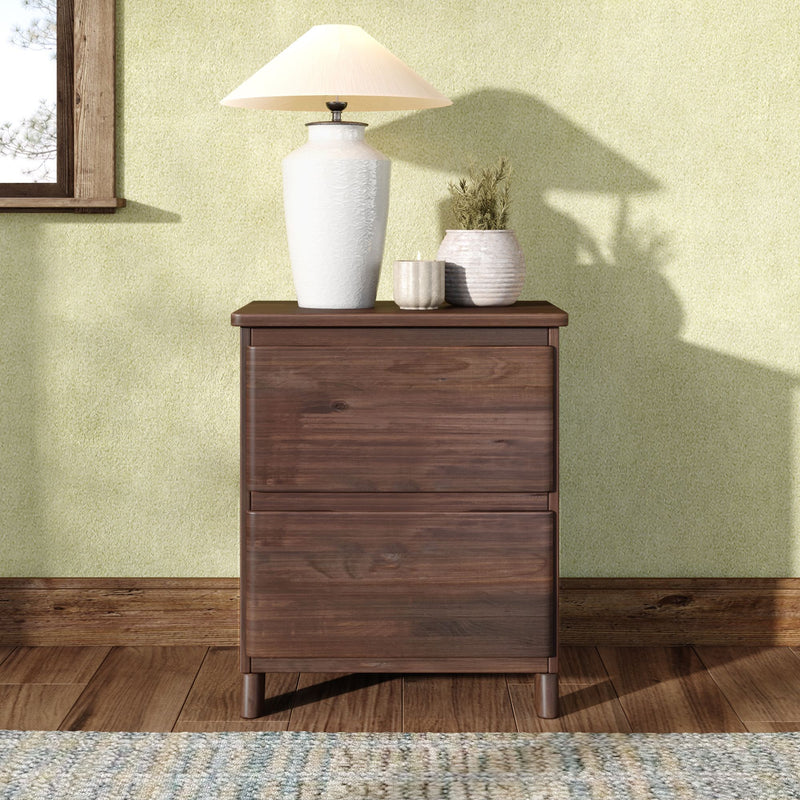 White ceramic table lamp on a dark wooden nightstand with textured vases, candle and potted plant by a wood-framed window against a soft green wall, rustic bedroom decor