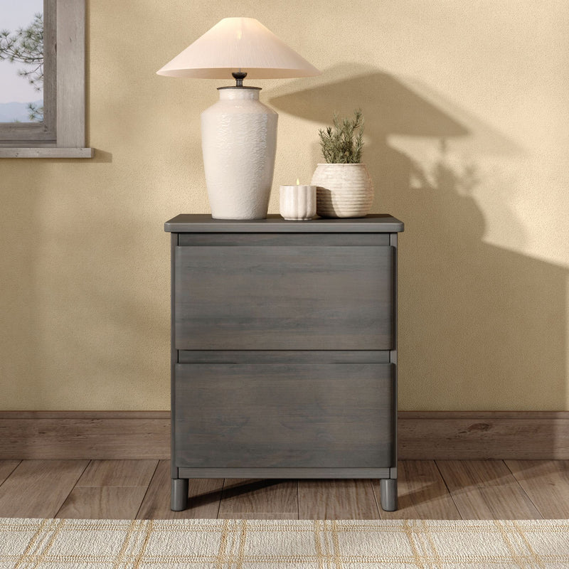Cozy farmhouse bedside scene: white ceramic table lamp on gray nightstand with potted greenery and candle against a beige textured wall