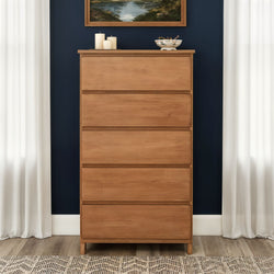Mid-century modern tall wooden dresser in natural oak, chest of drawers against a navy accent wall with white curtains and tabletop decor