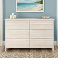 Whitewashed six-drawer dresser in coastal bedroom with blue wall, beach artwork, candles and decorative bowl on hardwood floor