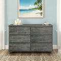 Gray distressed 6-drawer wooden dresser in coastal bedroom with beach wall art, decorative candles and bowl, hardwood floor and woven rug