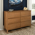 Mid-century modern light oak six-drawer dresser for bedroom storage against a navy accent wall with decorative candles, bowl, hardwood floors and patterned rug