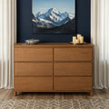Natural wood six-drawer dresser in a modern bedroom with navy accent wall, mountain artwork, decorative candles, white curtains