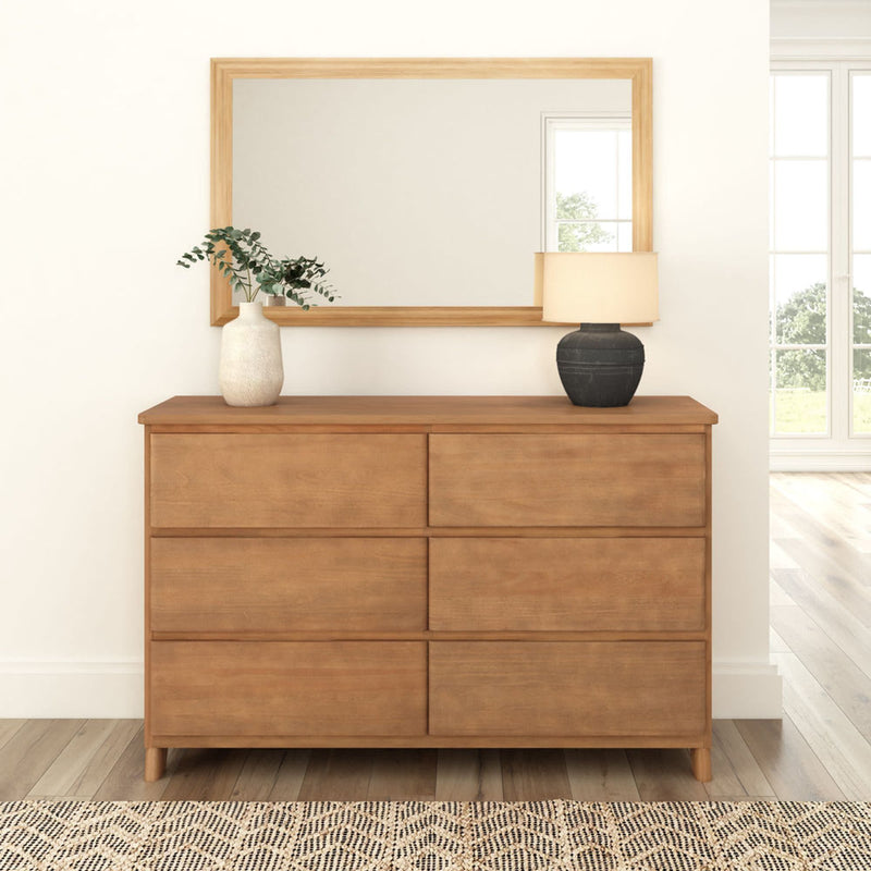 Mid-century modern wooden dresser with six drawers, topped with decorative vases and lamp, in bright minimalist bedroom.
