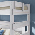 Whitewashed wooden twin-over-twin bunk bed with safety guardrails, beige mattress and blue striped pillow against a textured blue wall in a modern kids' bedroom