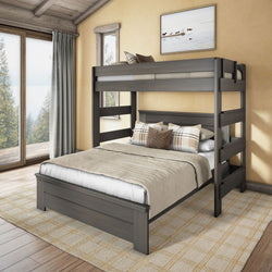 Gray wooden full-over-twin bunk bed in rustic cabin bedroom with neutral bedding, plaid accent pillows, area rug and large window overlooking forest