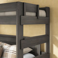 Gray stained solid wood bunk bed frame with safety guardrails and plaid accent pillows against a beige wall