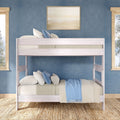 White wooden twin-over-full bunk bed in blue coastal-style bedroom with layered pillows, light-blue throw, woven jute rug and framed wall art