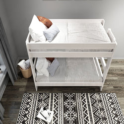 White wooden bunk bed with white and striped pillows in a modern bedroom featuring a geometric patterned black and white rug on hardwood floor.