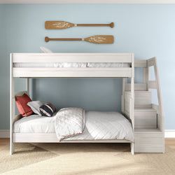 White wooden kids bunk bed with built-in stairs and coastal decor, light blue wall with decorative wooden oars, white quilt and navy-striped pillows
